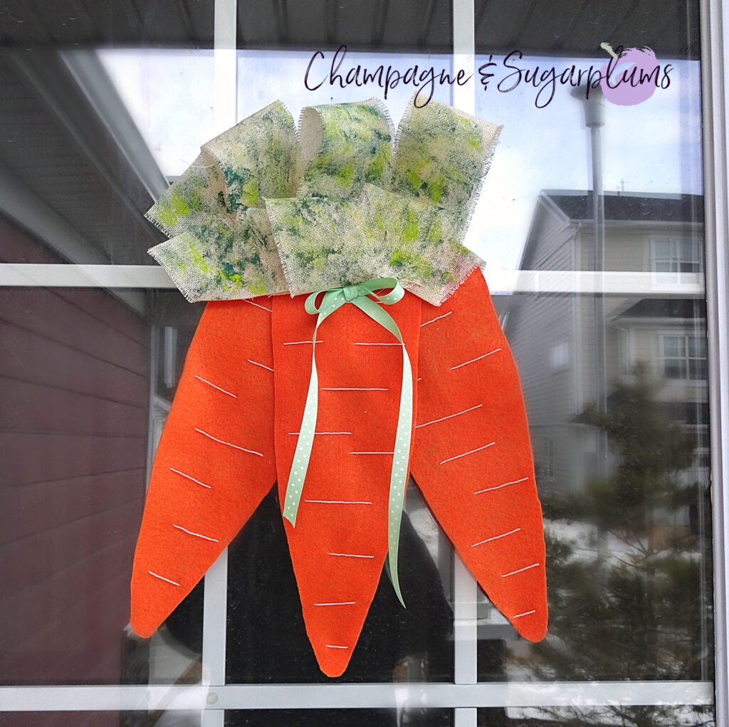 Completed carrot door decoration hanging on a window by Champagne and Sugarplums