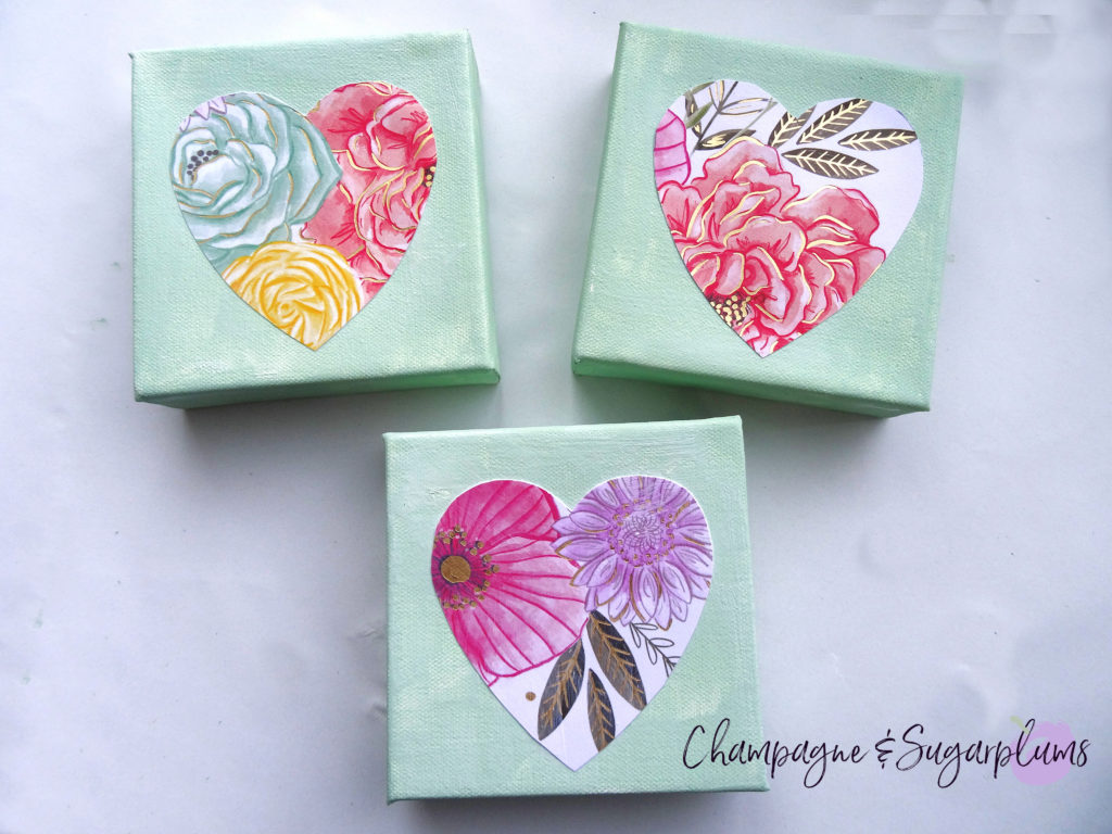 Three completed floral triptych canvases with paper hearts on a white background by Champagne and Sugarplums