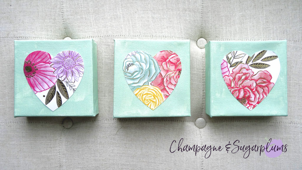 Three completed floral triptych canvases with paper hearts on a bench by Champagne and Sugarplums