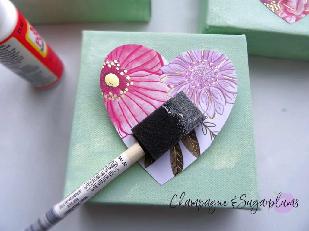 Gluing a paper heart onto a canvas with a foam brush by Champagne and Sugarplums