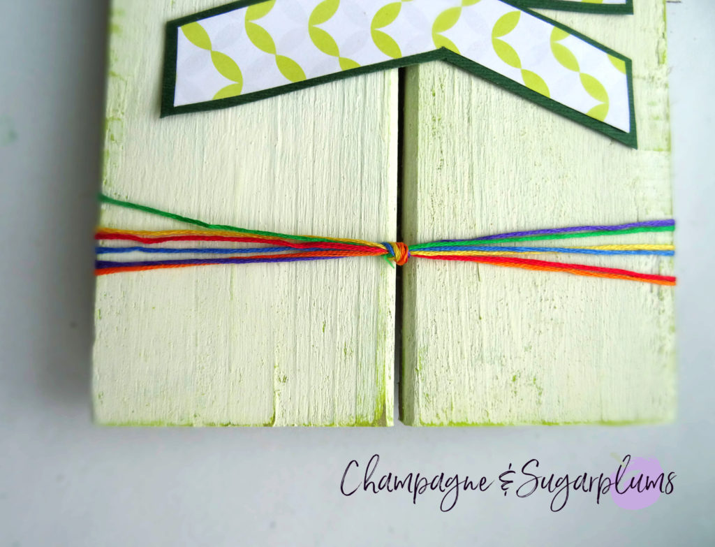 A rainbow of embroidery thread tied around the end of a wood plank by Champagne and Sugarplums