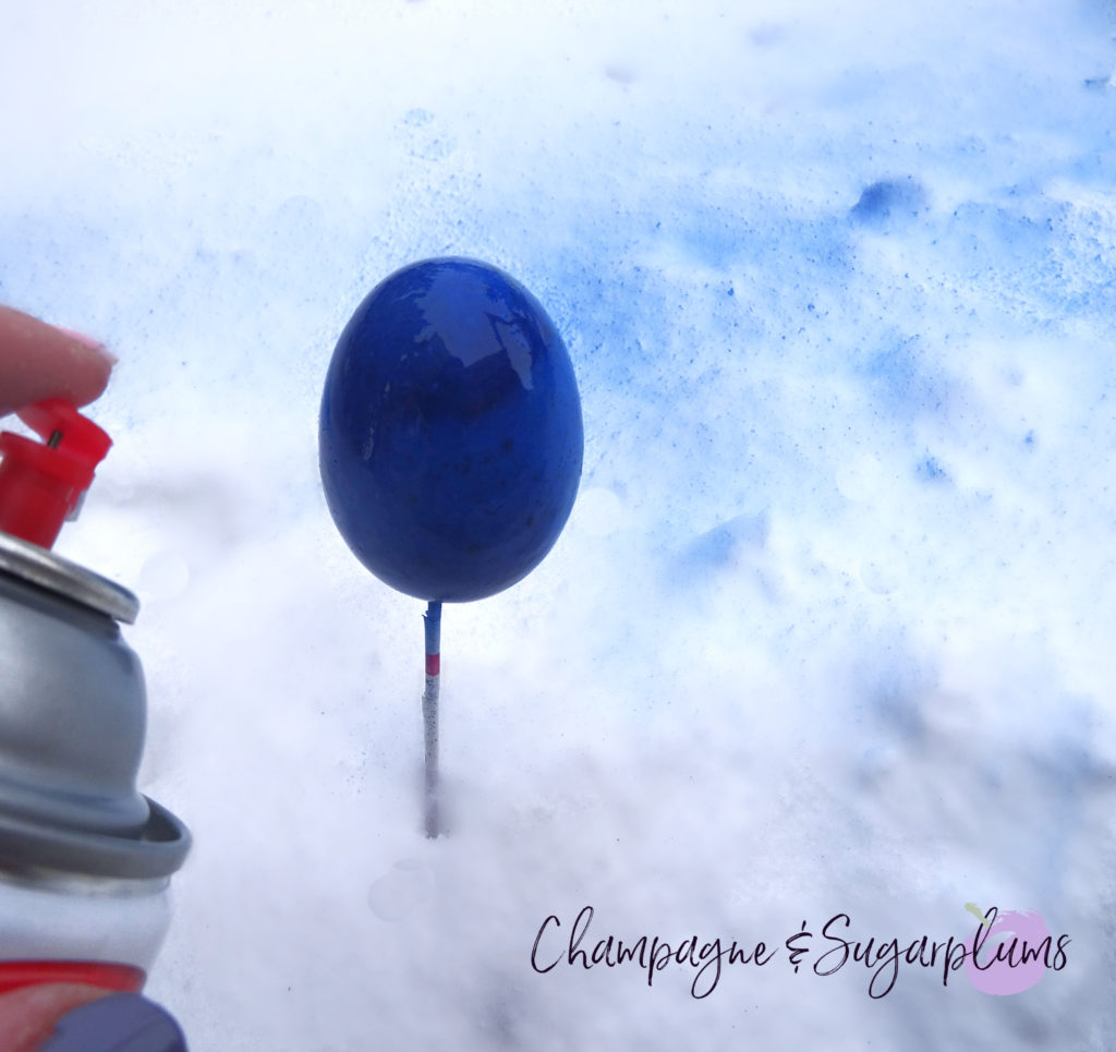 An egg being spray painted blue by Champagne and Sugarplums