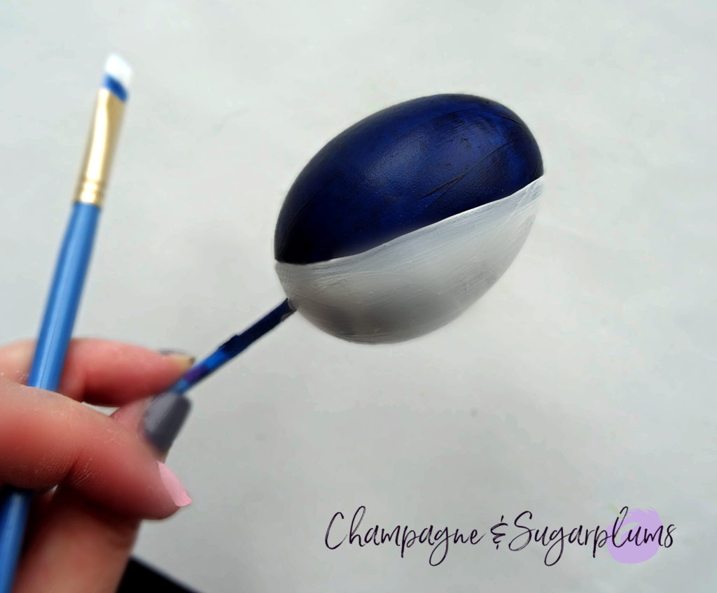 An egg being painted half white and half blue by Champagne and Sugarplums