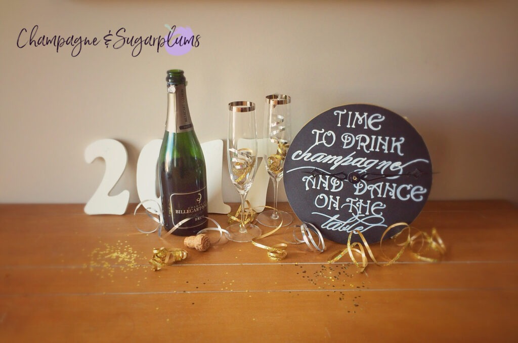 Countdown clock on a table with champagne glasses, bottle, ribbon and glitter by Champagne and Sugarplums
