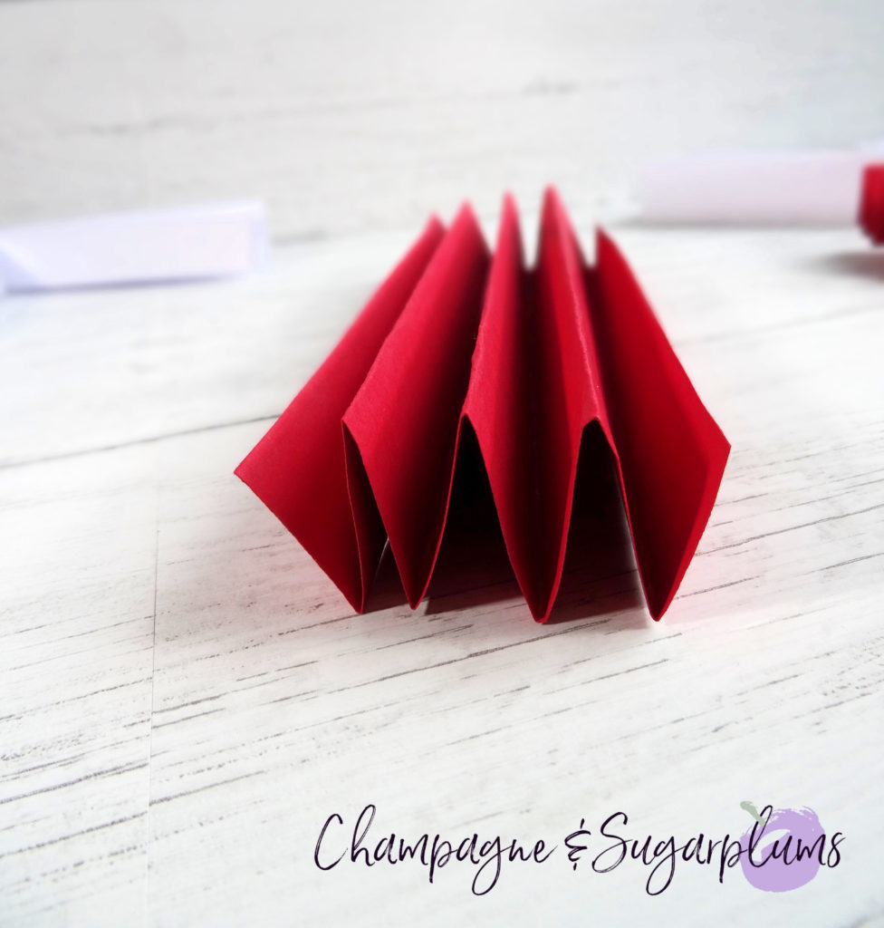 Red paper being folded it an accordion shape by Champagne and Sugarplums