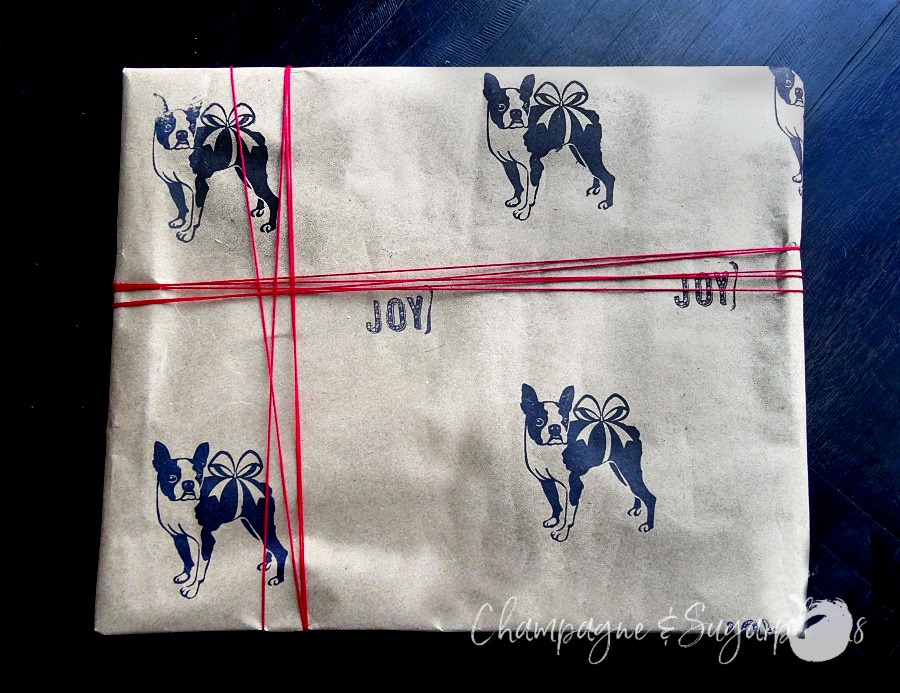 A gift wrapped in butcher paper stamped with Boston terriers with red twine around it by Champagne and Sugarplums