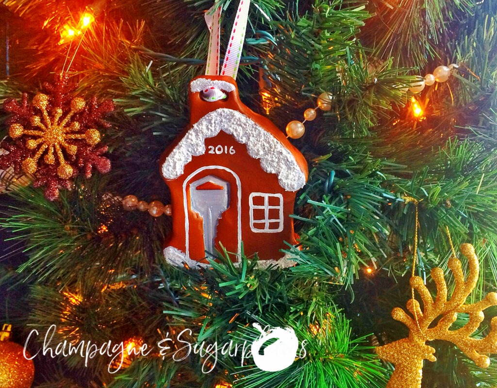 Gingerbread house ornament hanging on a tree by Champagne and Sugarplums