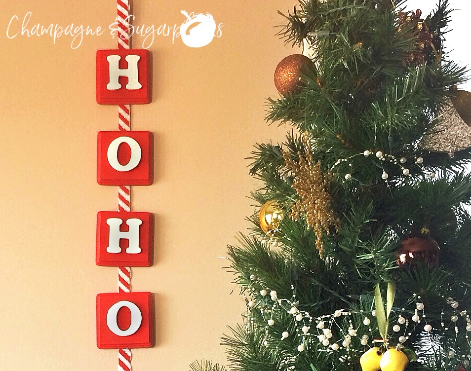 Christmas banner hanging on a wall beside a decorated tree by Champagne and Sugarplums