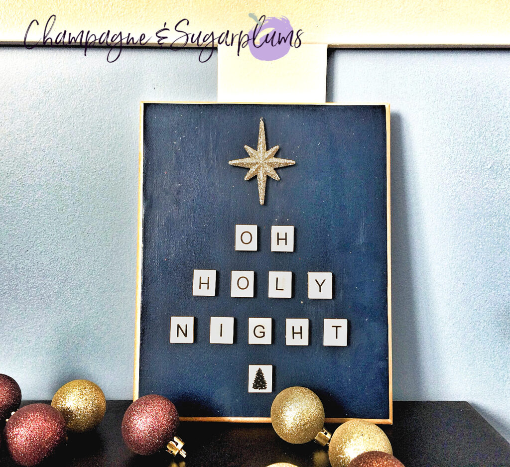 Letter tile plaque on a table with a blue wall with mini ornaments by Champagne and Sugarplums