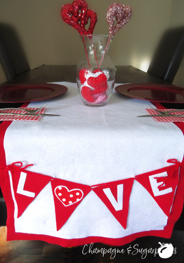 Love table runner on a dark table, with red plates and vase with hearts by Champagne and Sugarplums