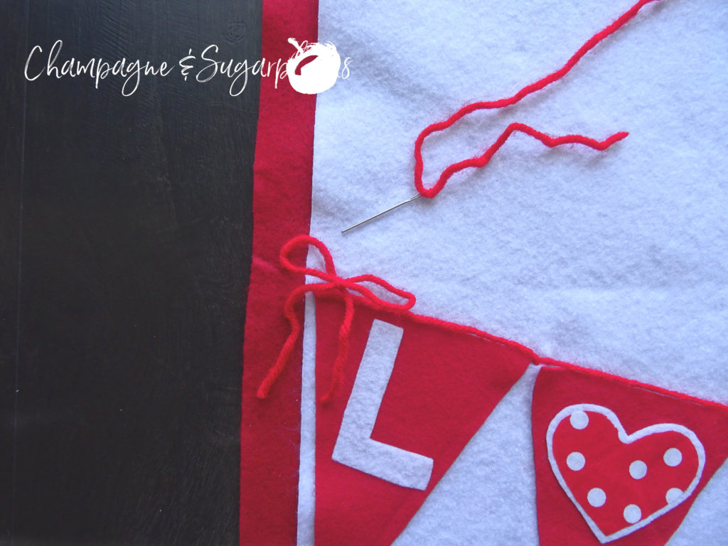 Red yarn bow attached to the corner of a felt flag on a Love table runner by Champagne and Sugarplums