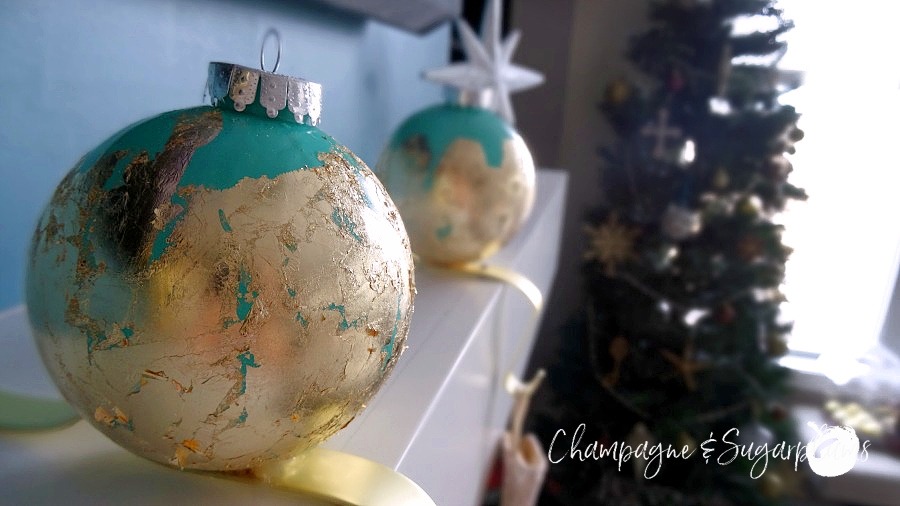 Ornament stocking holders on a white mantel surrounded by mini gold and brown ornaments with Christmas tree in the background by Champagne and Sugarplums