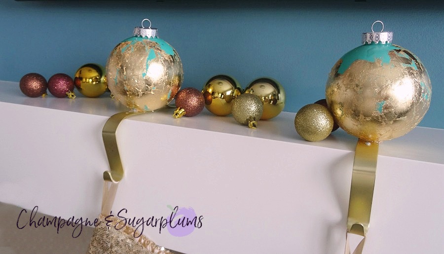 Ornament stocking holders on a white mantel surrounded by mini gold and brown ornaments by Champagne and Sugarplums