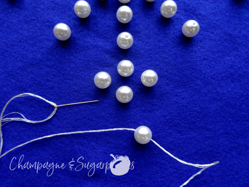 White pearl beads being hand sewn to royal blue felt by Champagne and Sugarplums