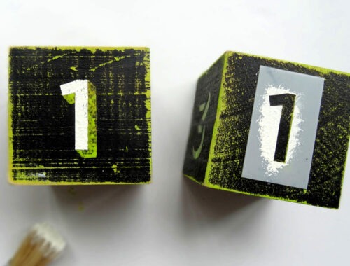 Two wooden blacks painted in black and green with the number one on them by Champagne and Sugarplums
