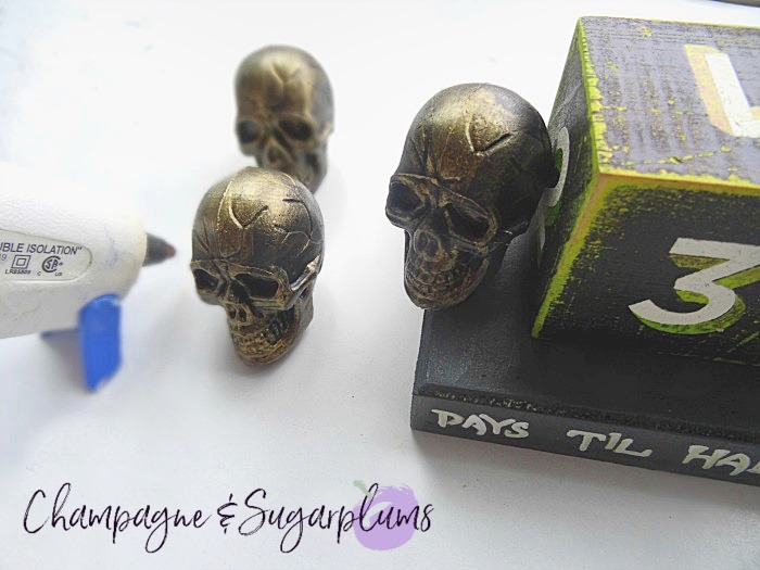 Gluing mini plastic skulls onto a wood block by Champagne and Sugarplums