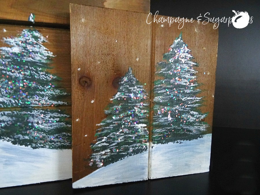 Painted holiday trees with glitter twinkle lights on wood planks by Champagne and Sugarplums