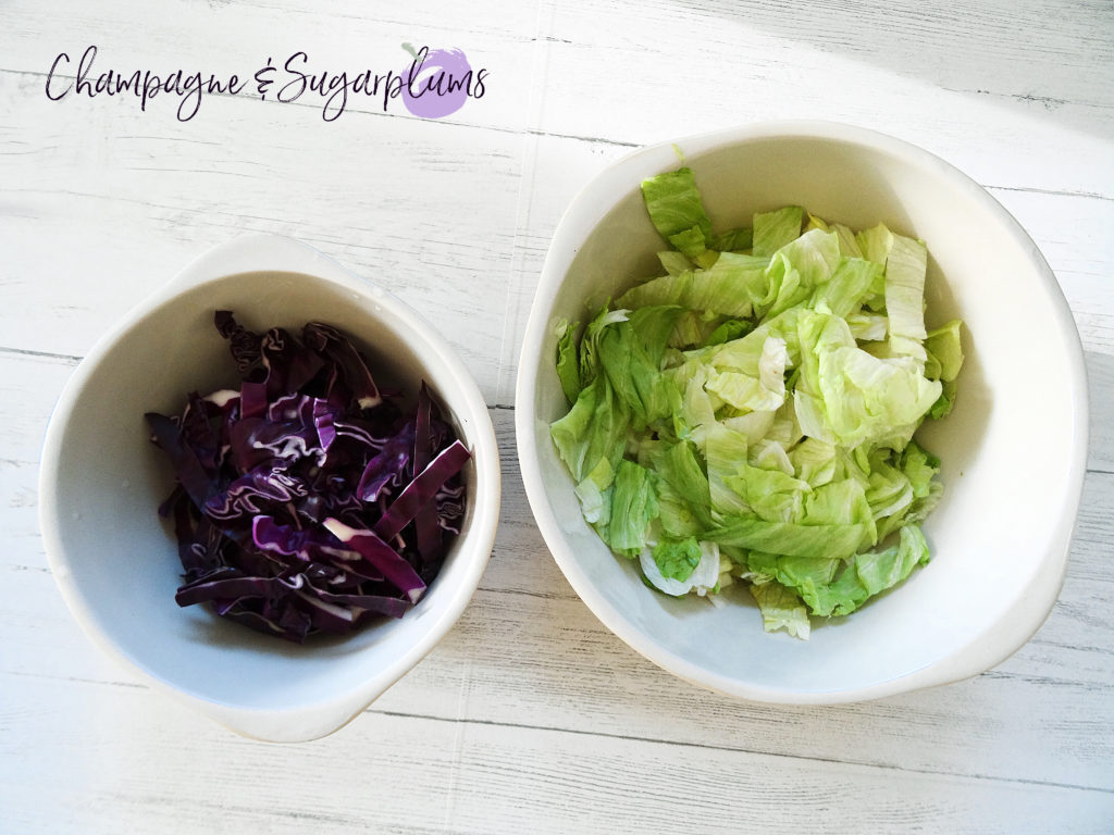 Shredded red cabbage and chopped lettuce in white bowls by Champagne and Sugarplums