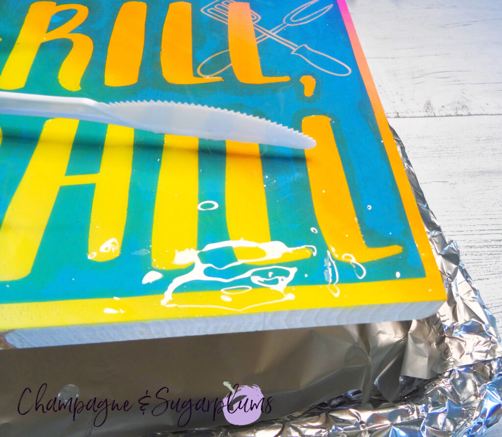 Spreading resin over a wood sign on a tray covered with tin foil by Champagne and Sugarplums