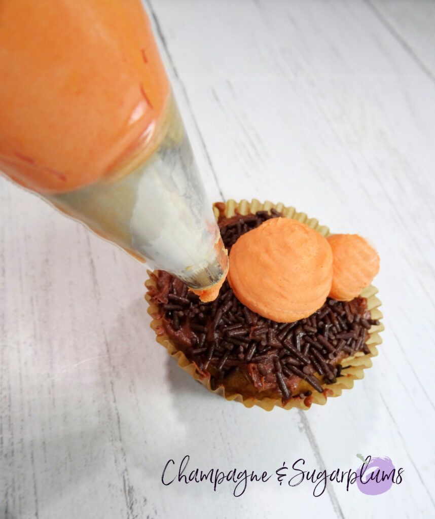 Piping three orange balls onto a cupcake on a white background by Champagne and Sugarplums