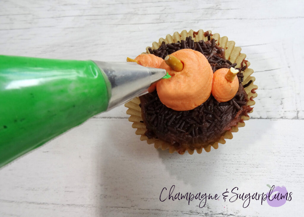 Piping green leaves onto an icing pumpkin on a white background by Champagne and Sugarplums