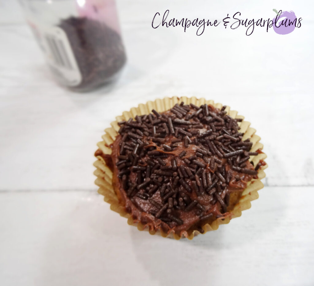 Iced cupcake with chocolate icing and sprinkles on a white background by Champagne and Sugarplums