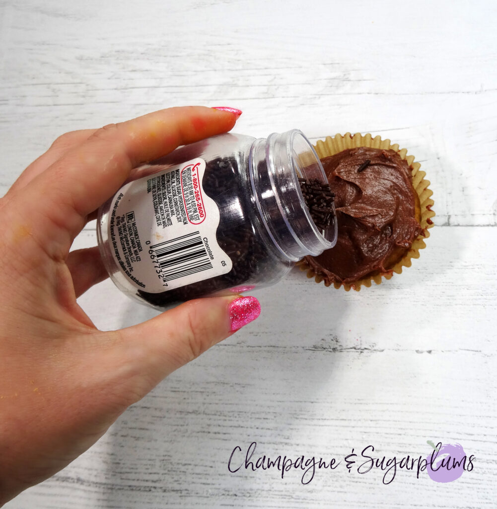 Adding chocolate sprinkles on top of an iced cupcake on a white background by Champagne and Sugarplums