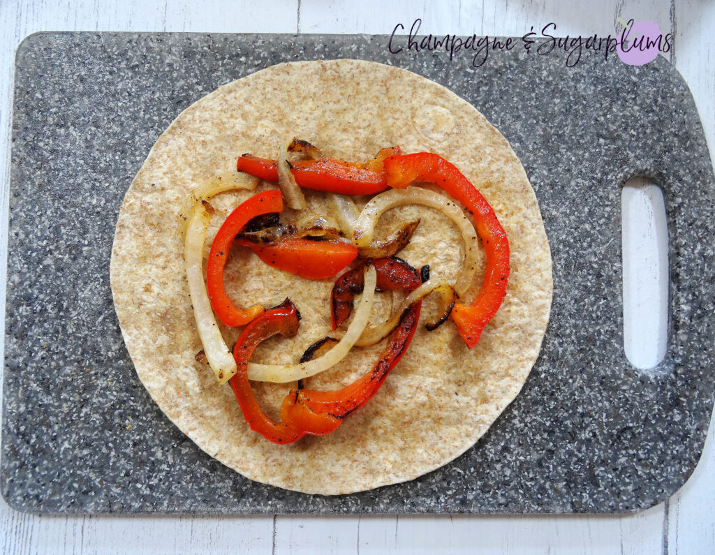 Adding onions and peppers to a quesadilla on a grey cutting board by Champagne and Sugarplums