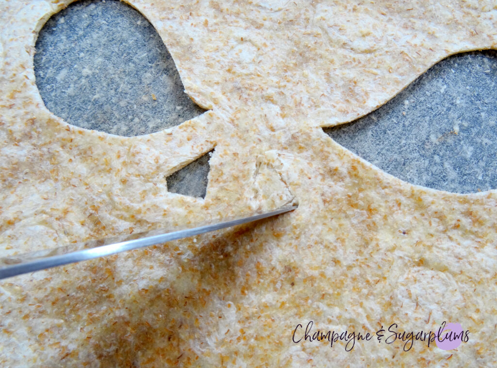 Cutting a nose into a tortilla on a grey cutting board by Champagne and Sugarplums