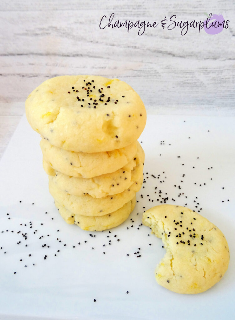 Lemon Poppy Seed Cookies stacked on a white plate, one cookie has a bite taken out of it, by Champagne and Sugarplums