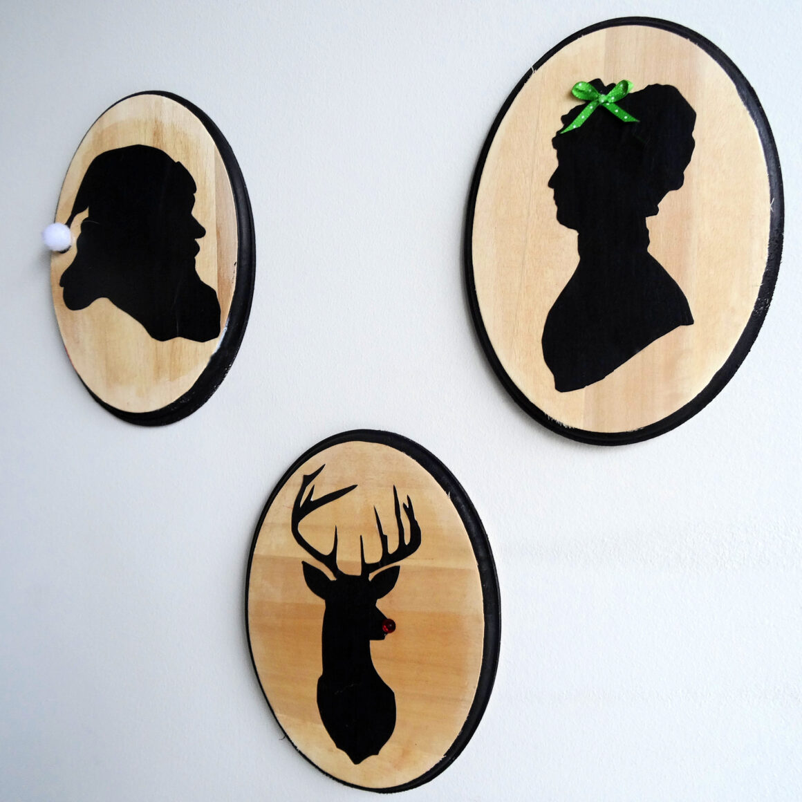 Three oval wood plaques with silhouettes of Santa, Mrs. Claus and Rudolf on a white background by Champagne and Sugarplums