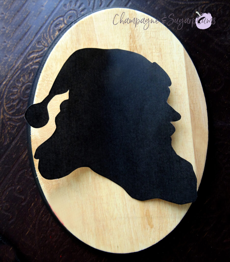 A black paper Santa silhouette sitting on an oval wood board by Champagne and Sugarplums