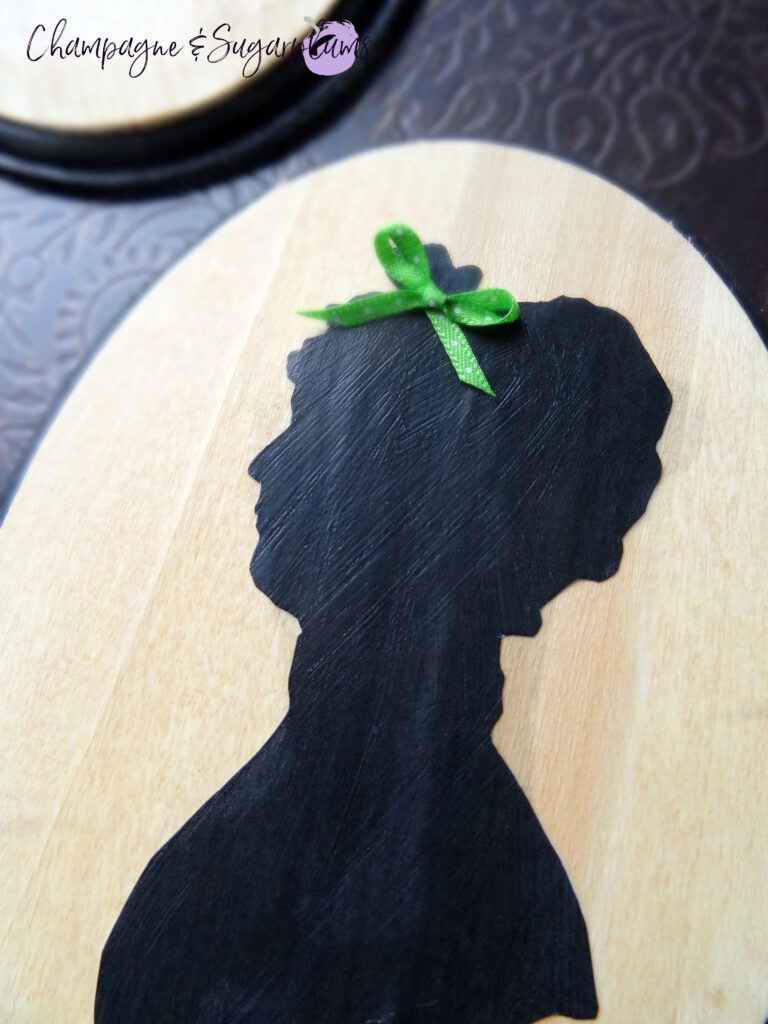 Adding a green bow to a Mrs. Claus silhouette on a wood board by Champagne and Sugarplums