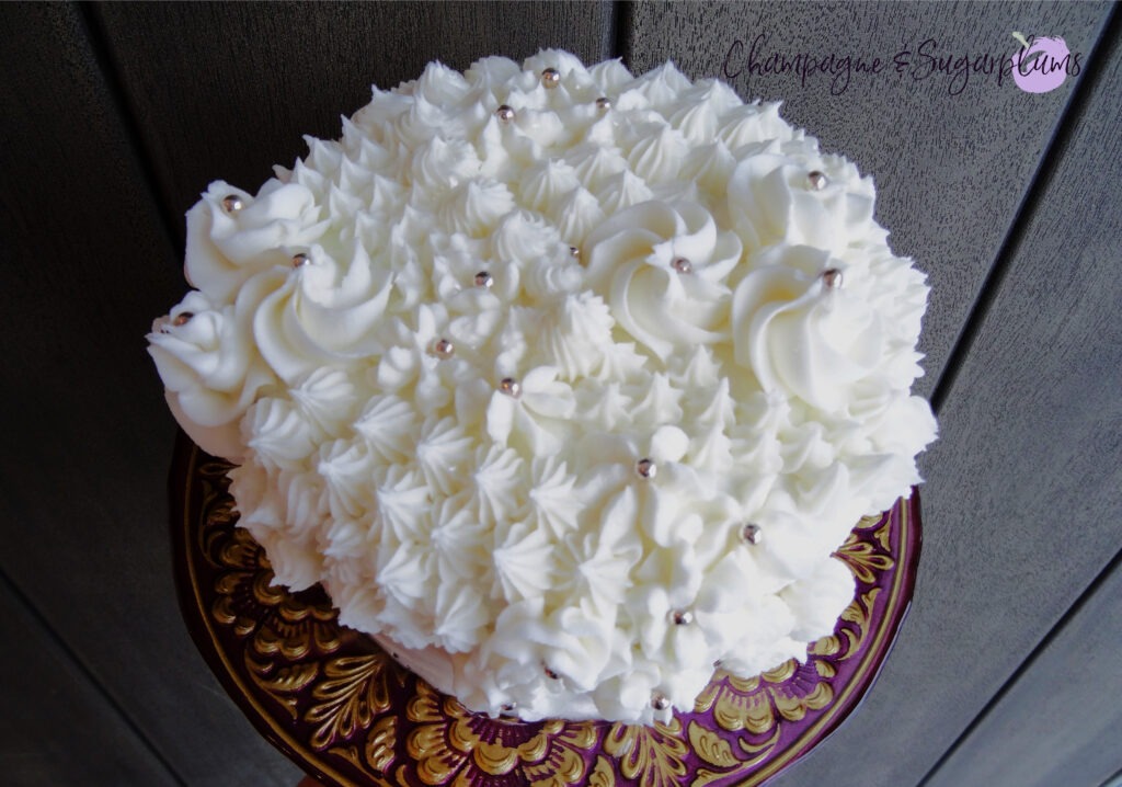 Champagne Cake sliced on a decorative stand in front of a wood background by Champagne and Sugarplums