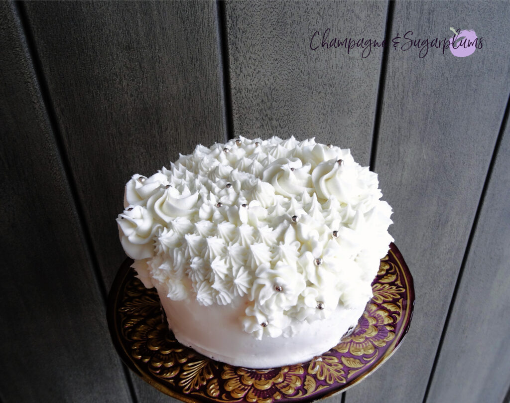 Champagne Cake sliced on a decorative stand in front of a wood background by Champagne and Sugarplums