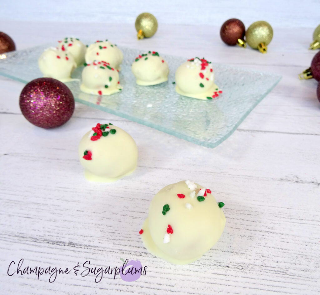 Natural Peanut Butter Snowballs on a glass plate surrounded by ornaments on a white background by Champagne and Sugarplums