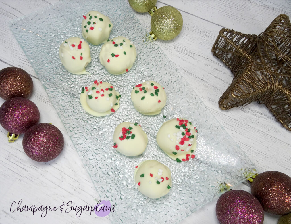 Natural Peanut Butter Snowballs on a glass plate surrounded by ornaments on a white background by Champagne and Sugarplums