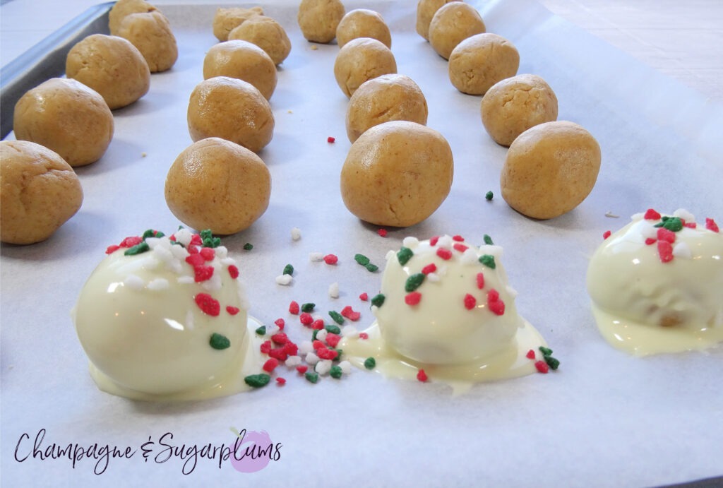Adding white chocolate and red and green sprinkles to Snowball treats on a baking tray by Champagne and Sugarplums