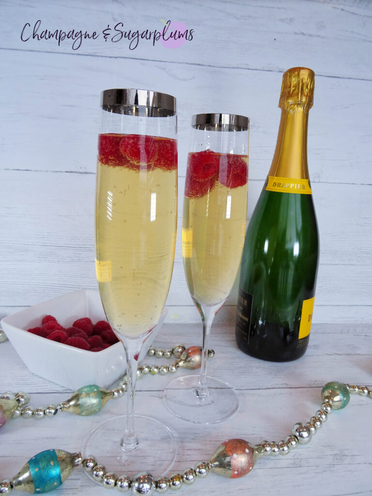 Drinks with raspberries in a champagne flute, beside a bottle on a white background by Champagne and Sugarplums