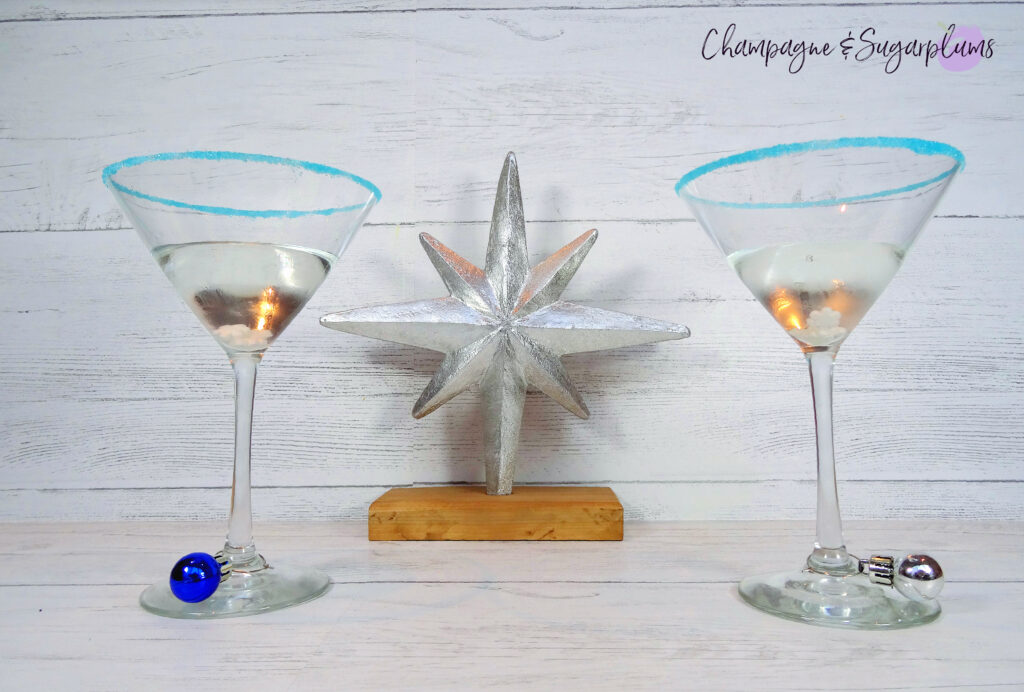 Polar Bear Martini cocktails, rimmed with blue sugar on a white background beside a silver star decoration by Champagne and Sugarplums