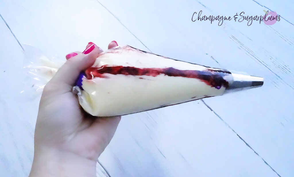 Cream cheese icing striped with pink colouring being held in an icing bag with large circle tip on a white background by Champagne and Sugarplums