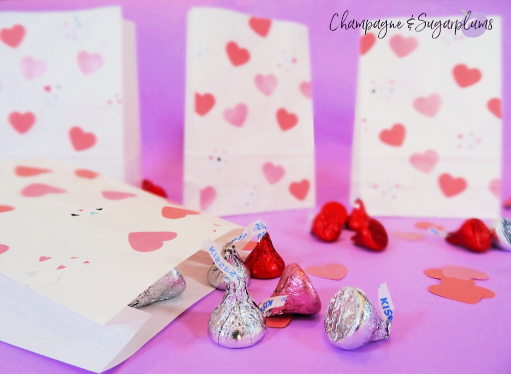 Valentine bags with pink hearts on purple background surrounded by chocolates and paper hearts by Champagne and Sugarplums