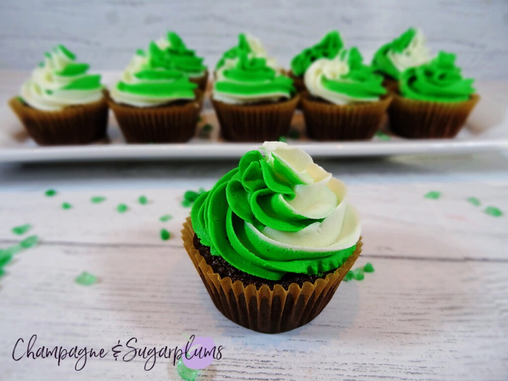 Chocolate cupcakes with peppermint frosting on a white plate with green sprinkles by Champagne and Sugarplums