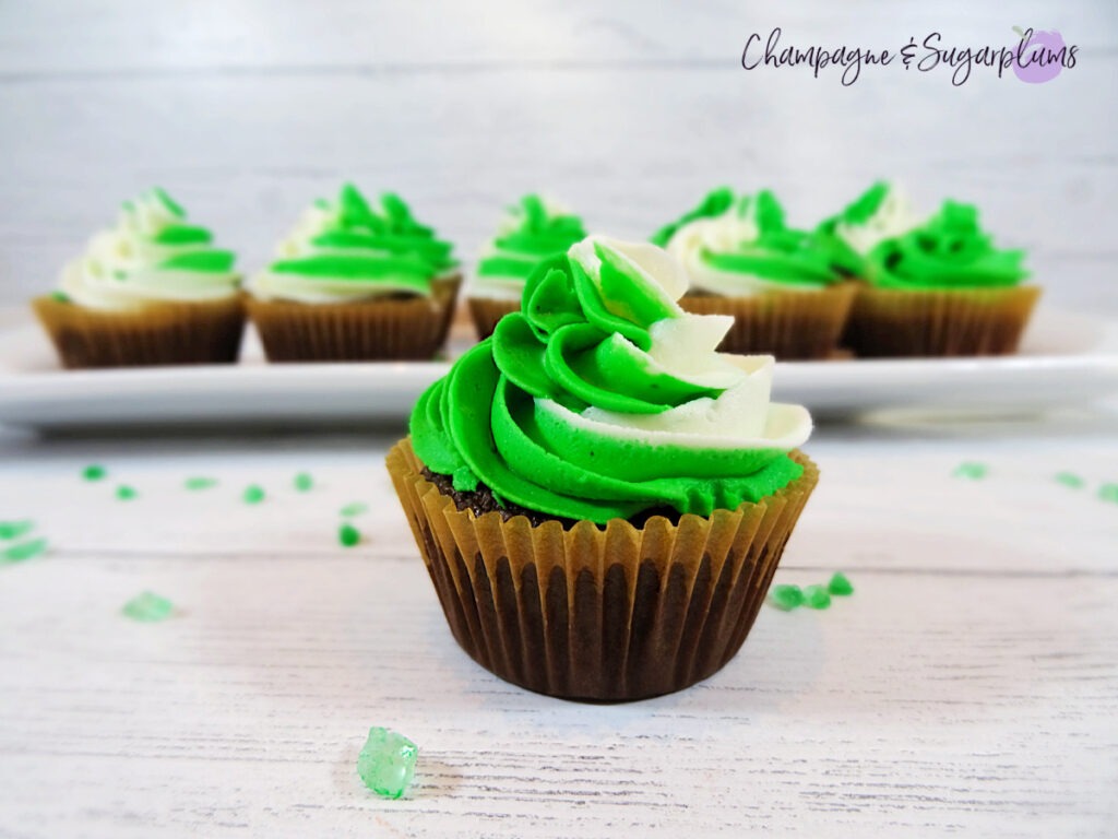 Chocolate cupcakes with peppermint frosting on a white plate with green sprinkles by Champagne and Sugarplums