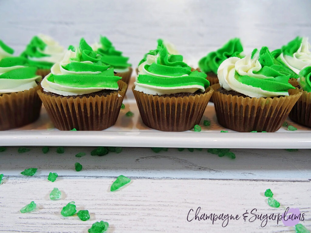 Chocolate cupcakes with peppermint frosting on a white plate with green sprinkles by Champagne and Sugarplums