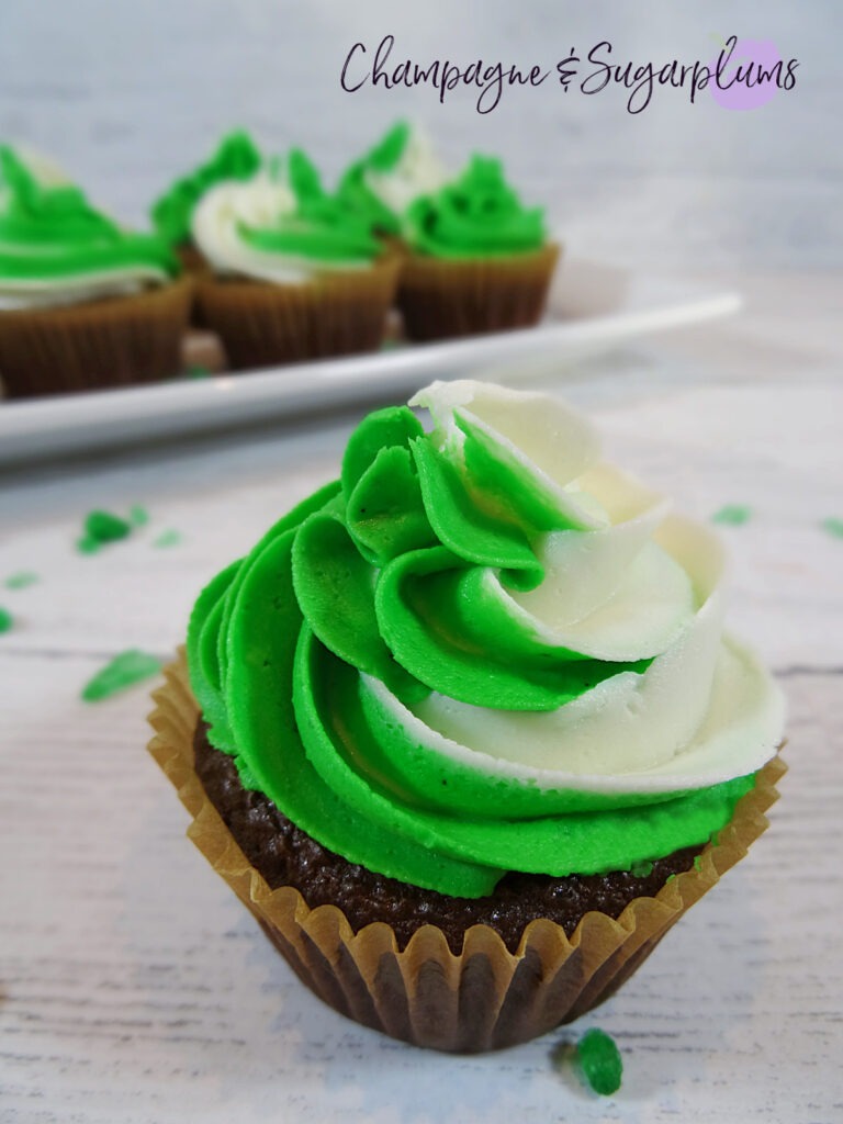 Chocolate cupcakes with peppermint frosting on a white plate with green sprinkles by Champagne and Sugarplums