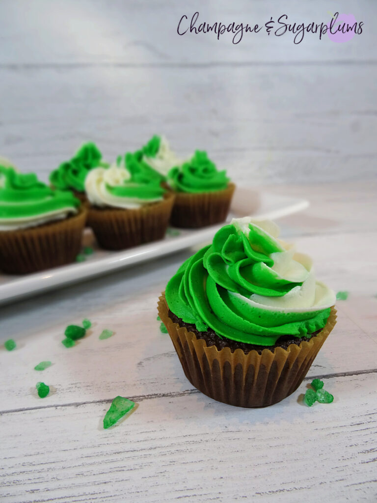 Chocolate cupcakes with peppermint frosting on a white plate with green sprinkles by Champagne and Sugarplums