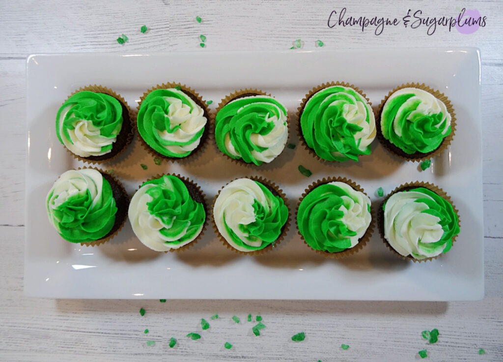 Chocolate cupcakes with peppermint frosting on a white plate with green sprinkles by Champagne and Sugarplums