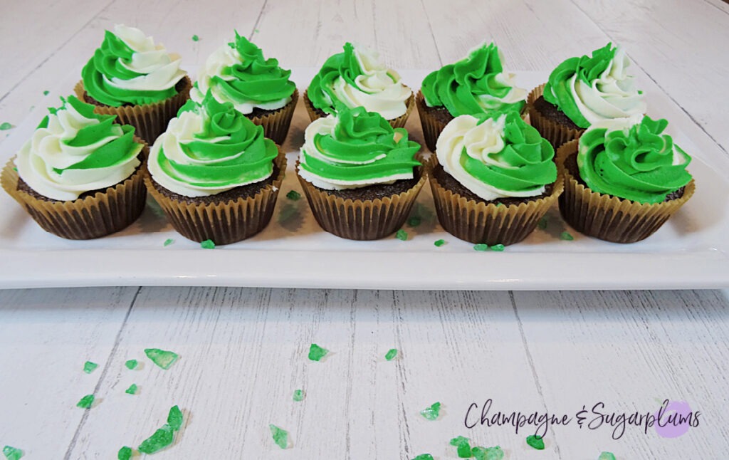 Chocolate cupcakes with peppermint frosting on a white plate with green sprinkles by Champagne and Sugarplums