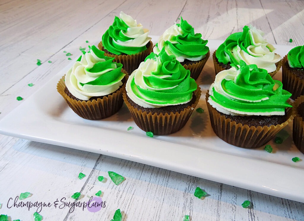 Chocolate cupcakes with peppermint frosting on a white plate with green sprinkles by Champagne and Sugarplums